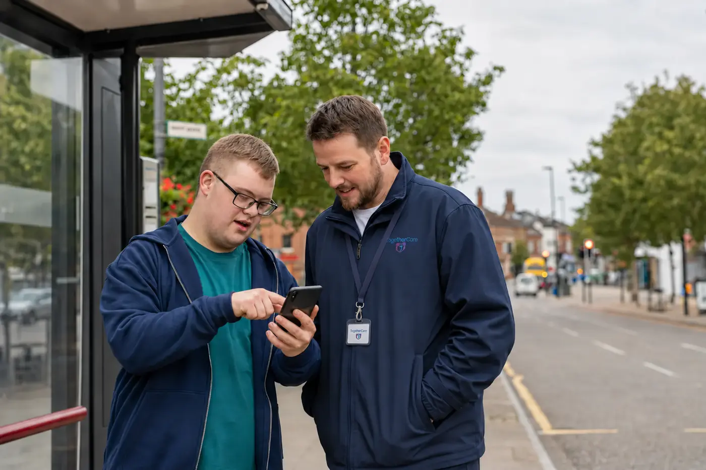A young adult and support worker using a phone together in the local community